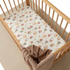 Diggers and tractors print organic fitted cot sheet on a wooden nursery cot styled with soft bedding and neutral tones