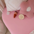 Bubblegum organic fitted cot sheet on a baby cot in a cosy nursery setting with warm pink tones and gentle textures
