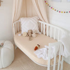 Snuggle Hunny Babyccino organic fitted cot sheet styled on a wooden nursery cot with soft neutral bedding and toys
