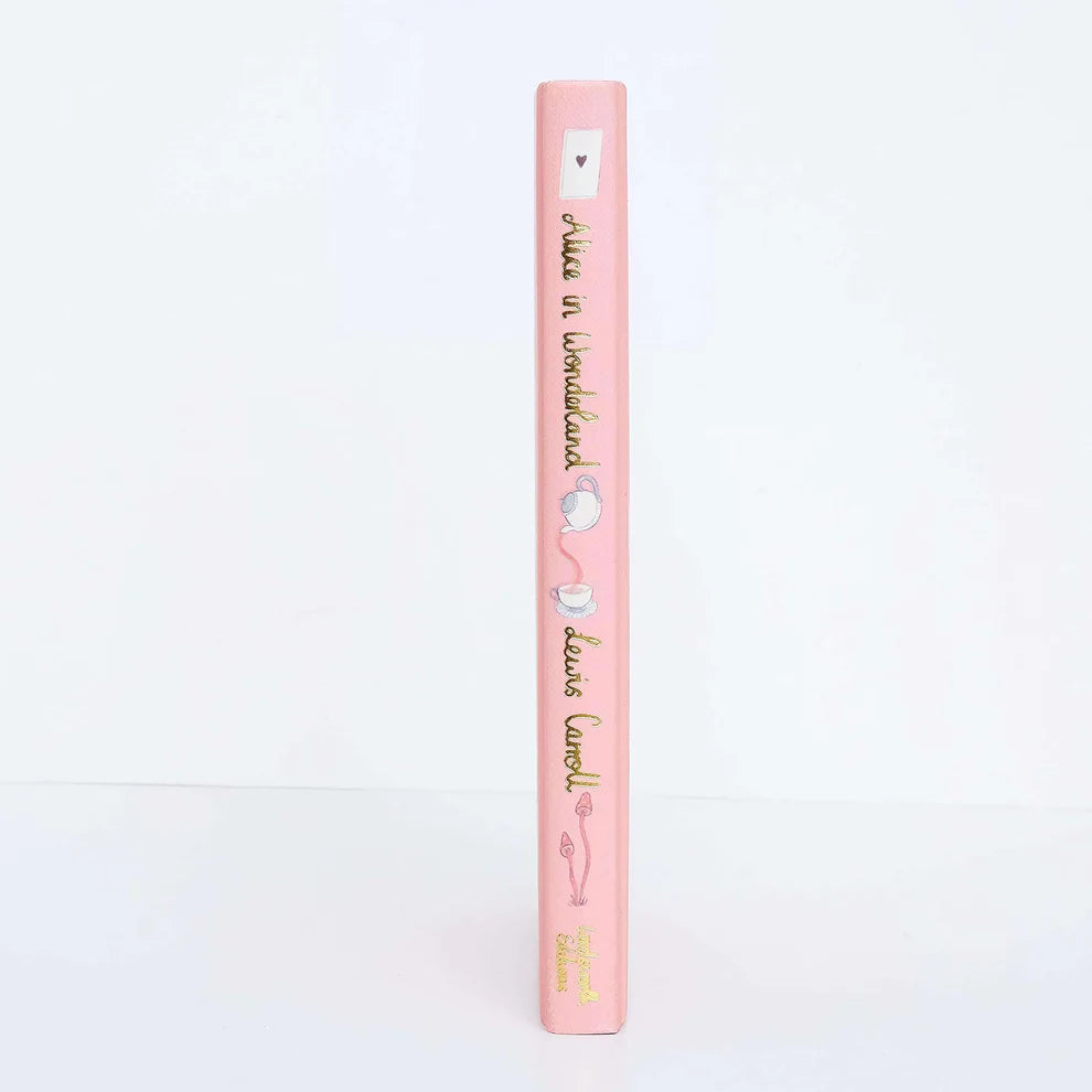 spine of Alice in Wonderland collector’s edition hardback book with blush pink illustrated cover, gold foil lettering and sprayed heart cards page edges by Lewis Carroll. wordsworth collectors limited edition