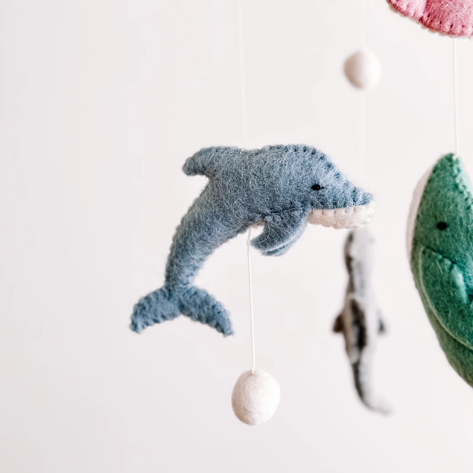 Felted dolphin toy hanging from a string against a white background