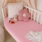 Snuggle Hunny Bubblegum organic fitted cot sheet styled on a nursery cot with soft pink bedding and plush toys