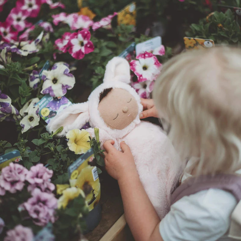 Child cuddling pink bunny Cozy Dinkum doll outdoors