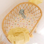 Beach Fun organic bassinet sheet fitted on a woven bassinet with yellow bedding creating a bright summer nursery look