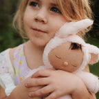 Child cuddling pink bunny Cozy Dinkum doll outdoors