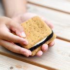 Hand holding a graham cracker with a chocolate filling on a wooden surface