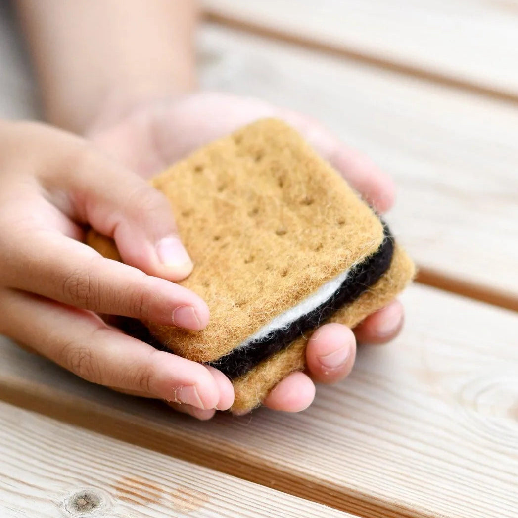Hand holding a graham cracker with a chocolate filling on a wooden surface