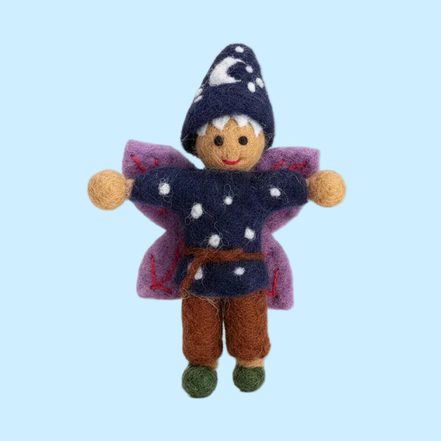 A small felted wool fairy doll with a navy blue hat decorated with white stars, a matching navy top with white polka dots, purple wings, brown pants, and green shoes, isolated on a white background.
