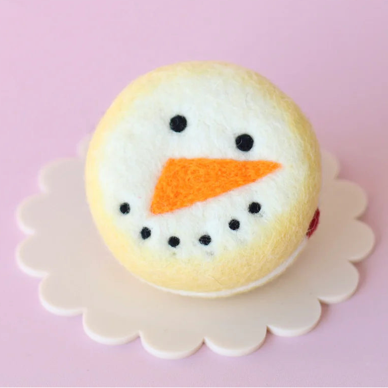 Snowman-themed cookie with black eyes and an orange carrot on a pink background