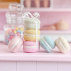Pastel-colored macarons stacked with a ribbon on a pink surface, blurred confectionery background