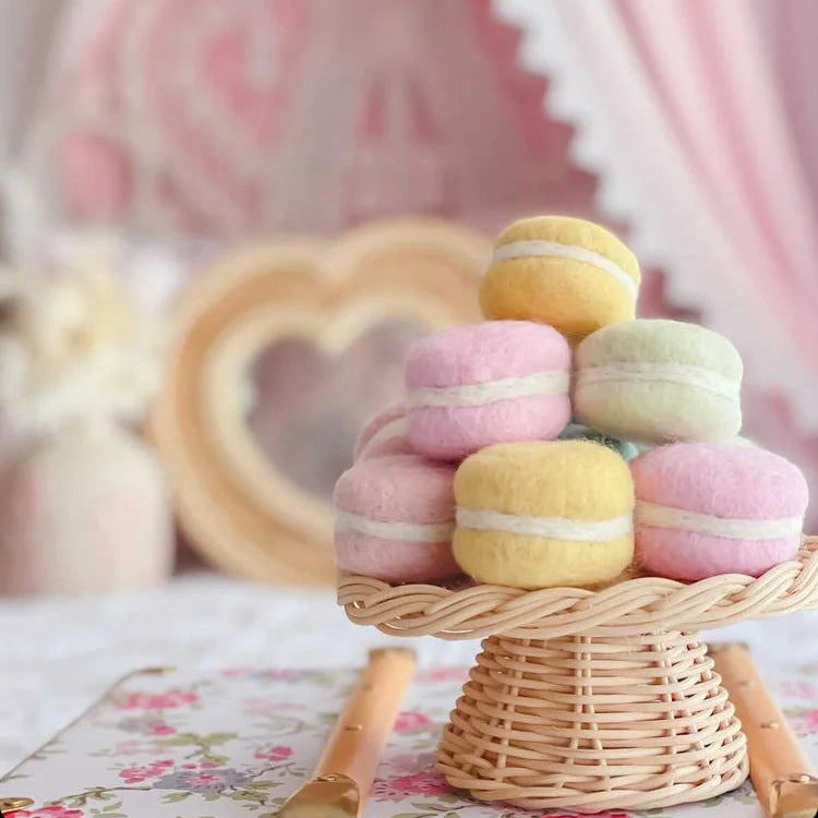 Pastel-colored macarons on a wicker stand with a soft pink background
